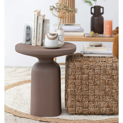 Stylish living room with modern brown table and woven ottoman, featuring books and a decorative vase on top.