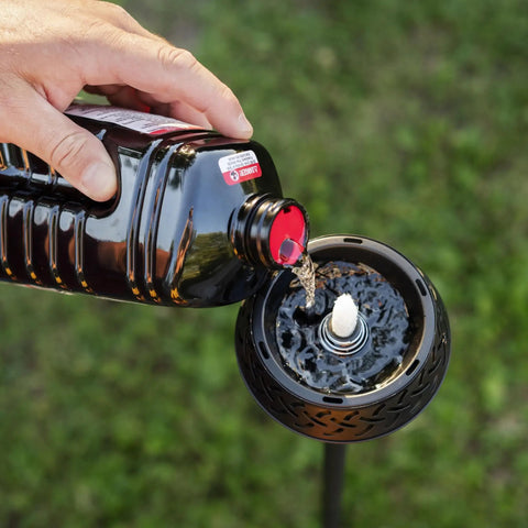 Pouring BiteFighter Mosquito Repellent Torch Fuel 64 Oz Citronella Cedar Formula for mosquito defense into torch outdoors