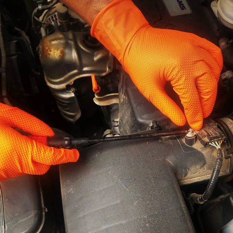 Close-up of TitanFlex orange nitrile gloves with raised diamond texture gripping a car engine component.
