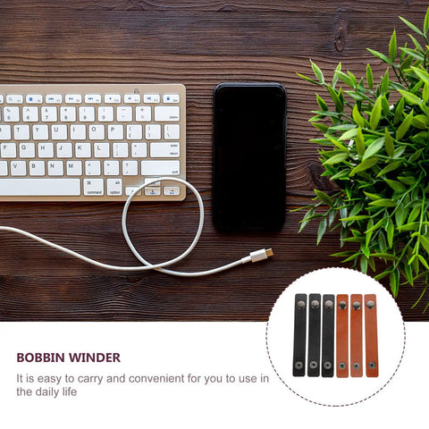 Six Piece Slick Leather Cable Straps For Usb Gadgets And Headphones Black Anti Tangle Wire Ties on a desk with keyboard and phone.