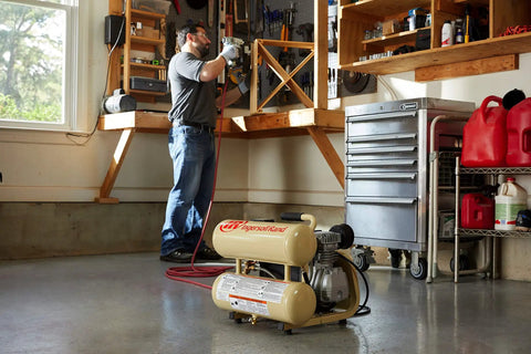 Man using the 2 HP Portable Twin Stack Air Compressor for shop work in a garage setting with tools around.