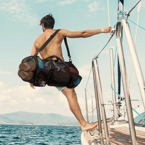 Man carrying 90L Mesh Duffle Bag For Scuba Gear And Snorkel Equipment on a boat, showcasing water sports beach essentials.