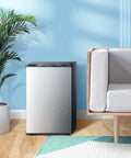 Top Tier Upright Mini Freezer With 3.0 Cubic Foot Storage And Brushed Stainless Steel Build beside a couch in a modern living room.