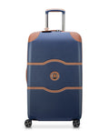 Delsey 26-inch spinner luggage in navy blue with faux leather accents and corner protectors, designed for durability and easy travel.