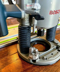 Guide Rail Adapter Fits Bosch 1617 Router Converts Plunge Or Fixed Base To Track Saw System For Dead On Cut Accuracy Uses Original Sub Base Screws For A No Sweat Install Designed And Built In America, close-up of Bosch router base on wooden surface.