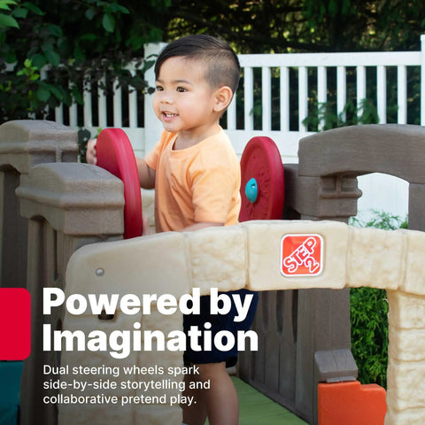 Child playing on Woodland Climber II Kids Playset With Toddler Slide And Climbing Wall, using dual steering wheels, backyard setup