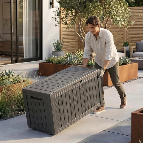 Person moving an 85 Gallon Outdoor Storage Box Resin Deck Box Waterproof UV Resistant With Reinforced Stability For Patio Garden And Poolside Striped Black Built To Last Storage For Cushions Toys And Tools on a patio.