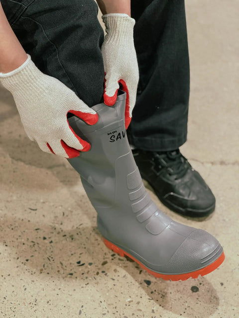 Person wearing Red Work Gloves Pack Of 300 Touch Screen Ready Latex Palm Coated Nitrile Safety Gloves adjusting gray boots.