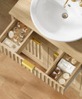 Kick Up Your Bathroom Style With This Slick Fluted Pedestal Sink Cabinet Featuring Two Doors And A Bottom Drawer In Natural Oak U Shape Cutout For Dope Space Saving Vibes, showcasing organized grooming items in drawers.