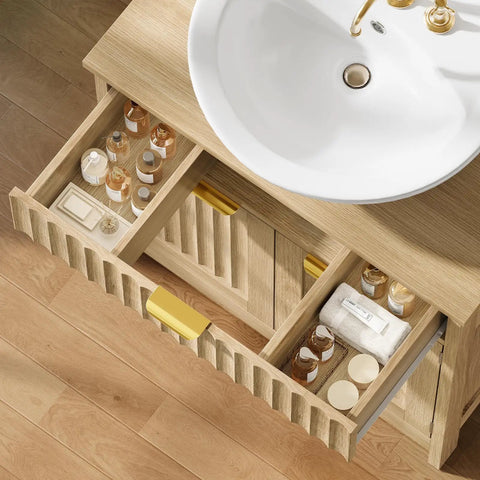 Kick Up Your Bathroom Style With This Slick Fluted Pedestal Sink Cabinet Featuring Two Doors And A Bottom Drawer In Natural Oak U Shape Cutout For Dope Space Saving Vibes, showcasing organized grooming items in drawers.