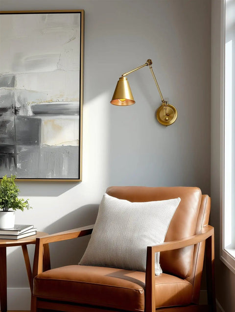 Gold vintage wall lamp with swing arm and conic shade above a leather chair in a modern living room.
