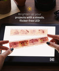 Hands holding film negative over LED Light Box 5x4 Inches For Negatives, Slides And Films, glare-free illuminated panel.