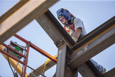 Welder wearing Wham 3030GB Solar Powered Welding Helmet With Pivot Headgear on metal beams at construction site