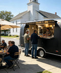 Turnkey Black Food Truck For Barbecue Catering Mobile Trailer With Handy Bathroom And Beefed Up Commercial Kitchen Setup For Legit Street Hustles On The Go serving customers outdoors.