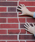 Hands pressing on a brick wall with visible gap filled by Tough 1/8 Inch Foam Backer Rod 16.4 Foot Gray Epdm Rubber Joint Filler.
