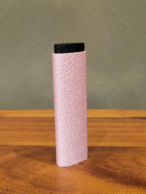 Reusable Skin File With Cover For Rock Climbing And Bouldering, pink textured surface with black cover, standing on a table.