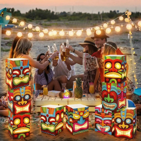 12 Pcs Hawaiian Luau Tiki Totem Gift Boxes With LED Lights For Outdoor Indoor Party Decor Vibrant Tropical Aloha Themed Gift Boxes For Tiki Bar Beach Parties And Survivor Themed Celebrations displayed at a beach party with string lights.