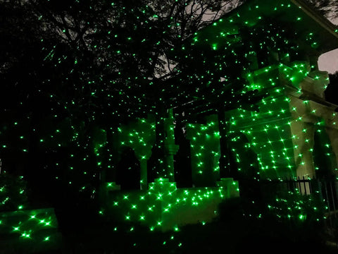 Outdoor display of Bluetooth Motion Laser Lights With Dope 7 Color Full Spectrum White Star Effects illuminating a house in green.