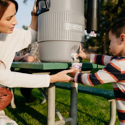 Five Gallon Portable Sports Cooler And Water Dispenser With Flat Seat Lid being used outdoors by woman and child