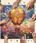 Hands assembling stained glass hot air balloon 1000-piece jigsaw puzzle city in the clouds scene that slaps for game night