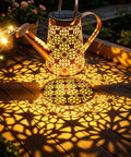 Solar Watering Can Lights, Large Retro Metal Hanging Outdoor LED Decor casting warm white patterns on a wooden deck.
