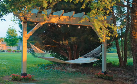 Outdoor hammock under a wooden pergola, surrounded by trees, featuring Outdoor Accents Mission Collection Decorative Post Base Covers on 6x6 posts.