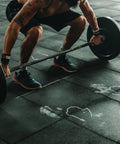 Person performing a deadlift exercise in a gym with barbell and weights on rubber flooring, wearing athletic gear.
