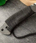 Close-up of Beast Fixed Blade Axe Knife With Saw Back And Sheath showing paracord-wrapped handle on speckled surface