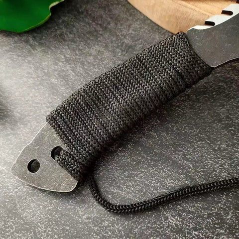 Close-up of Beast Fixed Blade Axe Knife With Saw Back And Sheath showing paracord-wrapped handle on speckled surface