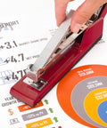 Hand placing Premium One Quarter Inch Staples, 210 Per Strip, Five Pack, 5000 Per Box in red stapler on office report.