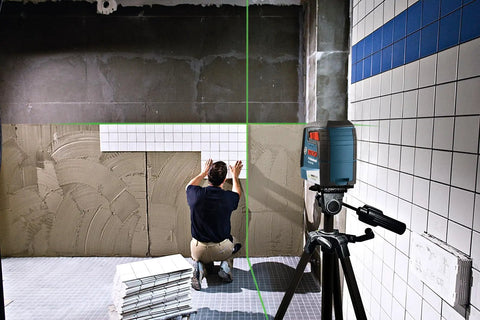 Man using Green Beam Self-Leveling Cross-Line Laser Kit With 40 Ft Range for precise tile alignment on construction site wall.