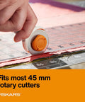 Hand using a rotary cutter on fabric, demonstrating 45mm Rotary Cutter Replacement Blades 5 Pack Ultra Sharp Precision Knives For Fabric Vinyl And Paper With Non Stick Coating For Smooth Cuts Heavy Duty Craft Supplies Perfect For Sewing Moms And Art Hustlers Who Demand Flawless Results.