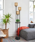 Boho Floor Lamp With Shelves And Three Lights in cozy living room, featuring rattan shades and acrylic shelf, next to gray sofa.