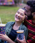 Couple enjoying iced coffee in Premium Neoprene Iced Coffee Sleeve, holds 22 to 28 oz cups, outdoor setting.