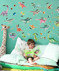 Child reading under dinosaur wall decals, featuring various colorful prehistoric creatures in a playful bedroom setting.