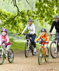 A family of four riding bicycles on a trail surrounded by green trees.