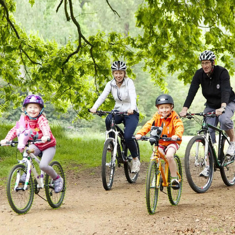 A family of four riding bicycles on a trail surrounded by green trees.
