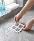 Fifty Pack Disposable Shower Drain Hair Catcher Stickers With Tough Adhesive Mesh Filter being applied to a drain.