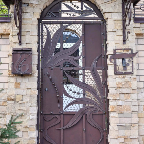 Decorative metal gate with intricate design set in a stone wall, suitable for Six Pack 4 Inch Bullet Weld On Hinges Set Heavy Duty Weldable Barrel Hinges Carbon Steel for Detachable Metal Swing Doors Gates Driveways Trailers and Ramps Ensures Secure Lids Easy Flipping and Durable Grilling.