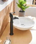 Oil Rubbed Bronze Vessel Sink Faucet With Waterfall Flow Tall One Hole Deck Mount Single Handle Vanity Faucet Includes Faucet Supply Hose Heavy Duty Solid Brass Construction Ceramic Cartridge For Leak Free Performance installed beside a white vessel sink on a wooden vanity.