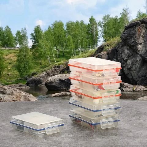 Pack of 6 clear mini fishing tackle boxes with 4 compartments, stacked by a scenic outdoor river setting