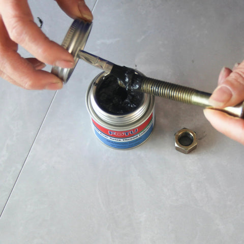 FOTU molybdenum disulfide grease anti-seize thread lubricant can, front view with lid open, coating a bolt beside a hex nut