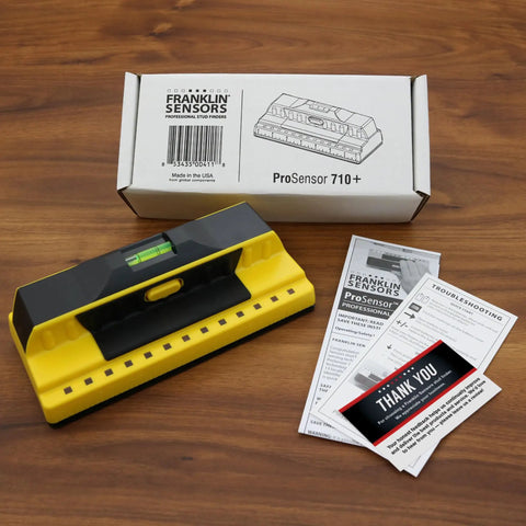 ProSensor 710 Plus Stud Finder With 13 Sensors, bubble level, packaging box, and instruction guides on wooden table