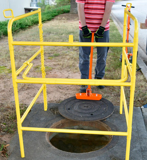 Person using Compact Magnetic Lid Lifter That Cracks Open Tough Manhole Covers Without Breaking A Sweat While Hauling Up To 150 Pounds Thanks To Strong Neodymium Magnets And Solid Aluminum Frame In Orange to lift a manhole cover.