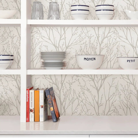 Kitchen with Treetops Peel And Stick Wallpaper In White And Off White visible behind white shelves with dishes and books