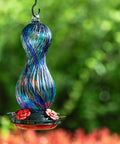 Outdoor Hand Blown Glass Hummingbird Feeder With 24 Oz Capacity And Four Feeding Ports in a garden setting