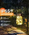 6 Pack Mason Jar Solar Lanterns With Jars And Hangers, Outdoor Waterproof Fairy Lights, glowing in rain on a garden path.