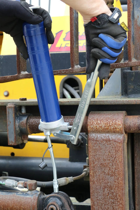Lincoln 1142 lever-action grease gun, blue metal body with 6-inch extension on rusted machinery.