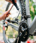 Bicycle repair scene: hand using screwdriver on derailleur near chainring on gray frame.