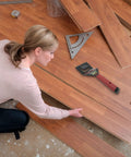 Person using Floor Lifter Pro Demolition Tool for easy removal of hardwood floors, showing tool placement and floor pieces.